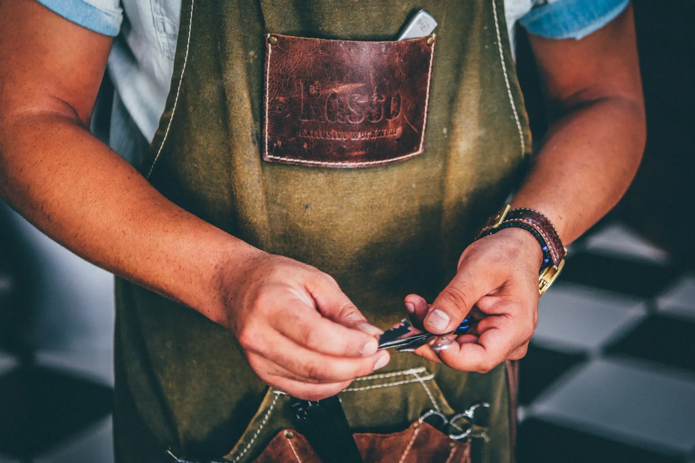 Person wearing a green apron with a leather patch at an outdoor event, holding a small tool or object in their hands.