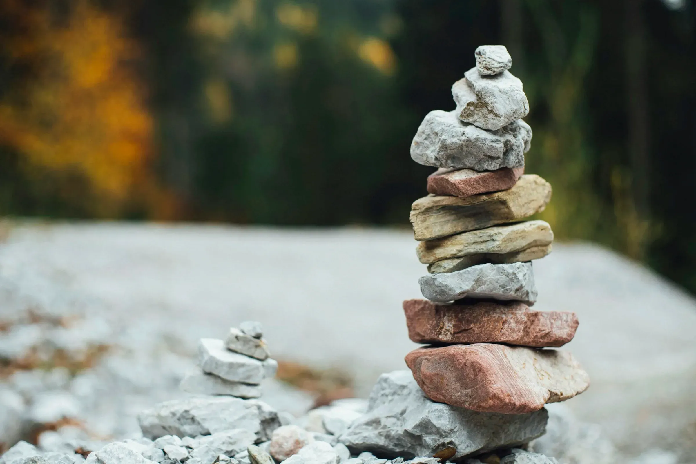 Stacked rocks in a natural outdoor setting with a blurred background of trees with autumn foliage.