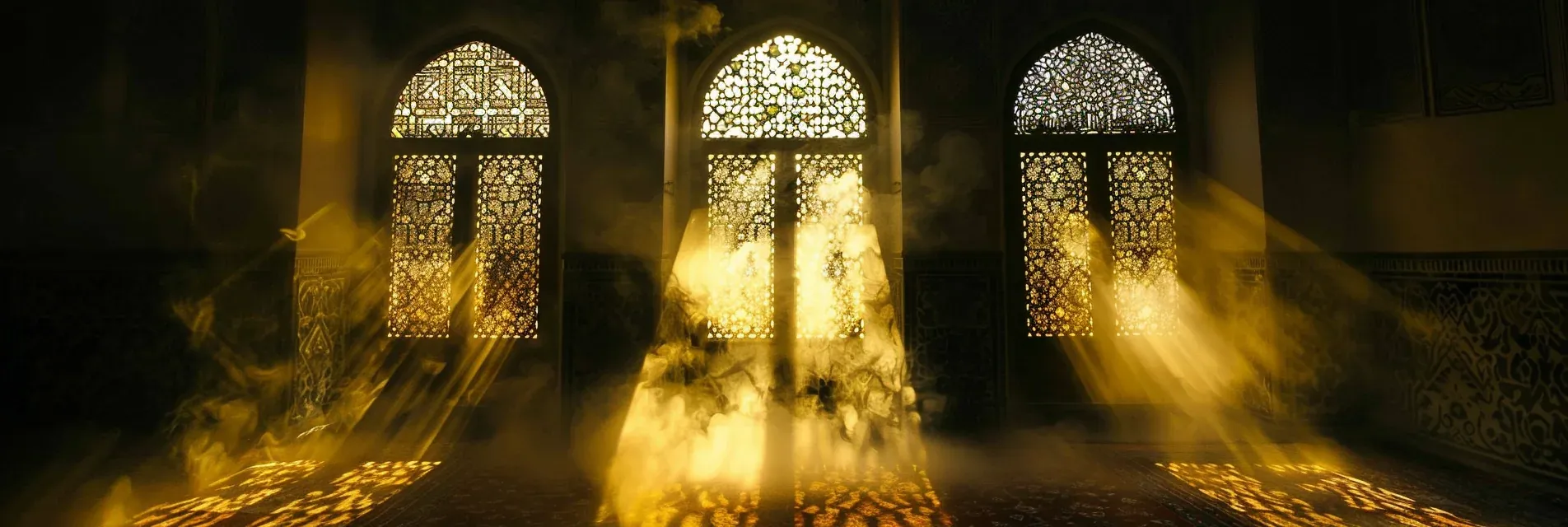 Sunlight streaming through intricately patterned stained glass windows inside a mosque, creating light and shadow effects on the interior walls and floor.